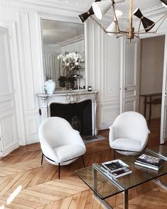 a living room with two chairs and a table in front of a mirror on the wall