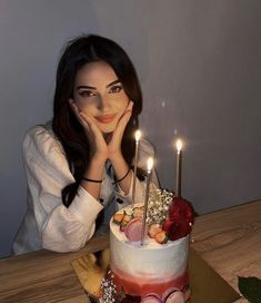 a woman is sitting in front of a cake with candles on it and her hand near her face