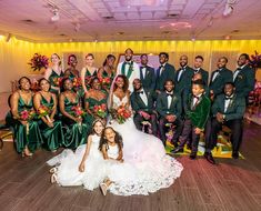 a large group of people dressed in green and white posing for a wedding photo on the dance floor