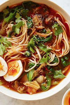 a white bowl filled with noodles, vegetables and hard boiled eggs on top of a table