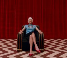 a woman sitting in a chair with red curtains behind her