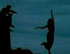 the silhouettes of two people on top of a building with one person reaching up into the air