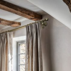 an open window with curtains hanging from it's sides and a wooden beam in the corner