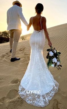 the bride and groom are walking in the sand dunes at sunset, holding each other's hands