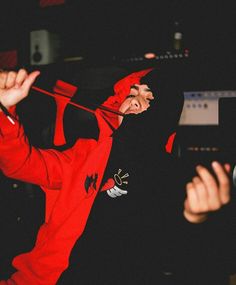 a man in a red hoodie and black jacket with his hands up to the side