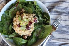 a white bowl filled with spinach salad and topped with cranberry sauce on top