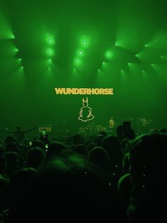 a large group of people standing in front of a stage with green lights and the words wunderhorse on it