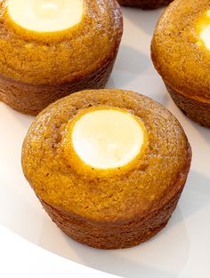 four muffins with butter on top are sitting on a white plate, ready to be eaten