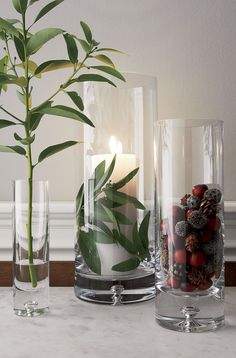 three glass vases filled with plants and candles on a marble counter top next to each other