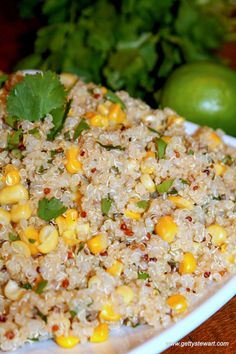 a white plate topped with rice covered in corn and cilantro next to limes