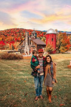 a man, woman and child standing in front of a barn with autumn foliages