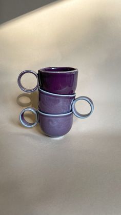 three purple coffee mugs stacked on top of each other with their handles extended to the side