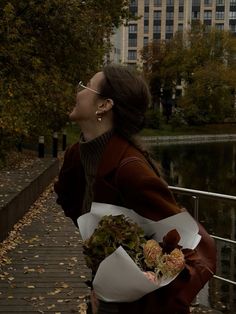 a woman is standing on a bridge with flowers in her hand and looking up into the sky