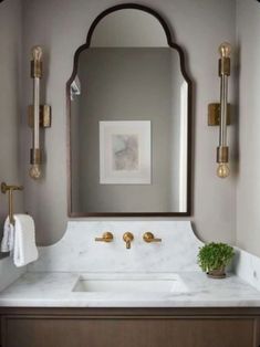 a bathroom vanity with marble counter top and gold faucet, mirror above it