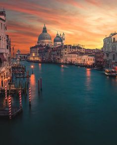 the sun is setting in venice, italy as boats go down the canal at dusk