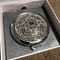 a silver pocket watch sitting in a box on the floor with its lid open to show it's intricate design