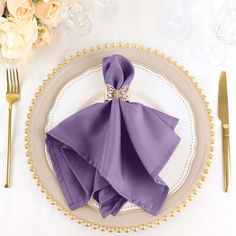 a place setting with purple napkins and silverware on a white table cloth covered plate