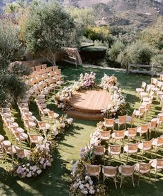 an outdoor ceremony setup with wooden chairs and flowers on the ground, surrounded by greenery