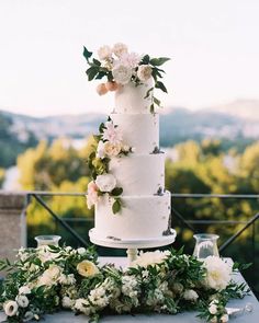 a white wedding cake sitting on top of a table covered in flowers and greenery