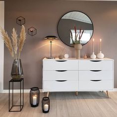 a white dresser sitting next to a mirror on top of a wooden floor covered in candles