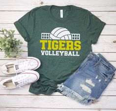 a t - shirt that says tigers volleyball next to ripped jeans and sneakers on a white wooden background