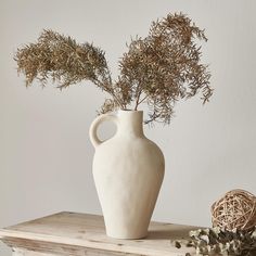 a white vase sitting on top of a wooden table next to dried flowers and a wicker basket