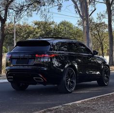 a black suv is parked on the side of the road near some trees and bushes