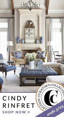 a living room with blue and white furniture, chandelier and fireplace in the background