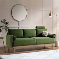 a green couch sitting on top of a wooden floor next to a table and lamp