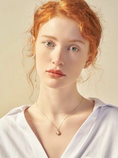 a young woman with red hair wearing a white shirt and holding a necklace on her neck