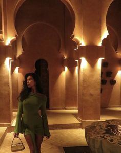 a woman in a green dress is walking through a room with arches and lights on the walls