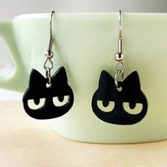 black cat earrings with white eyes on a coffee cup in front of a teacup