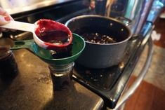 a person is spooning something out of a saucepan on the stove with another pan in the background