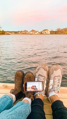 two people sitting on a dock with their feet crossed and one person holding a cell phone