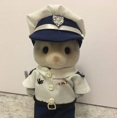 a teddy bear dressed as a police officer in blue and white uniform with a diamond brooch on it's head