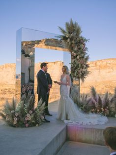 a bride and groom standing in front of a mirror during their wedding ceremony at sunset