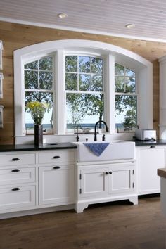 a kitchen with white cabinets and an arched window over the sink is pictured in this image