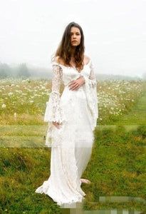 a woman standing in a field wearing a white dress with long sleeves and an open shoulder