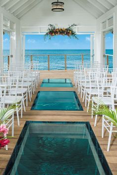 an indoor swimming pool with white chairs and flowers in the center, overlooking the ocean