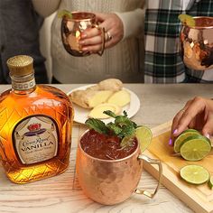 a person holding a glass filled with liquid next to a wooden cutting board and some limes