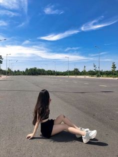 a woman sitting in the middle of an empty parking lot with her feet on the ground