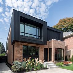 a modern house with black siding and brick walls, surrounded by greenery on the front lawn