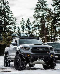 two trucks are parked in the snow near some trees