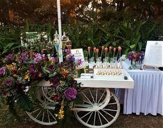 a table with flowers and desserts on it in front of some trees at an outdoor event