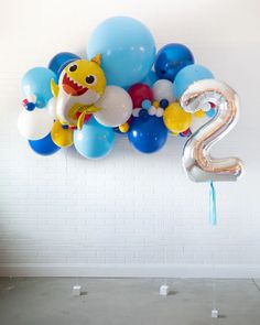 balloons are floating in the air next to a number two balloon wall hanging on a white brick wall