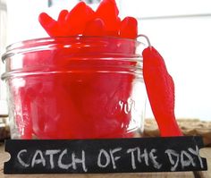 a jar filled with red gummy bears sitting on top of a wooden table next to a sign that says catch of the day