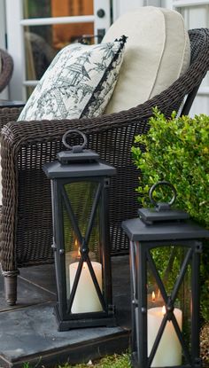 two lit candles sitting on top of a table next to a wicker chair and side table