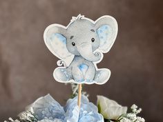 an elephant cake topper sitting on top of a bouquet of flowers and blue carnations