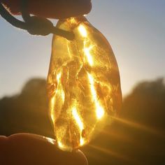 a person holding a glass piece with yellow lights in it's hand and the sun shining behind them