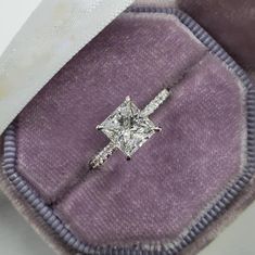 an engagement ring sitting on top of a purple velvet case with a white diamond in the center